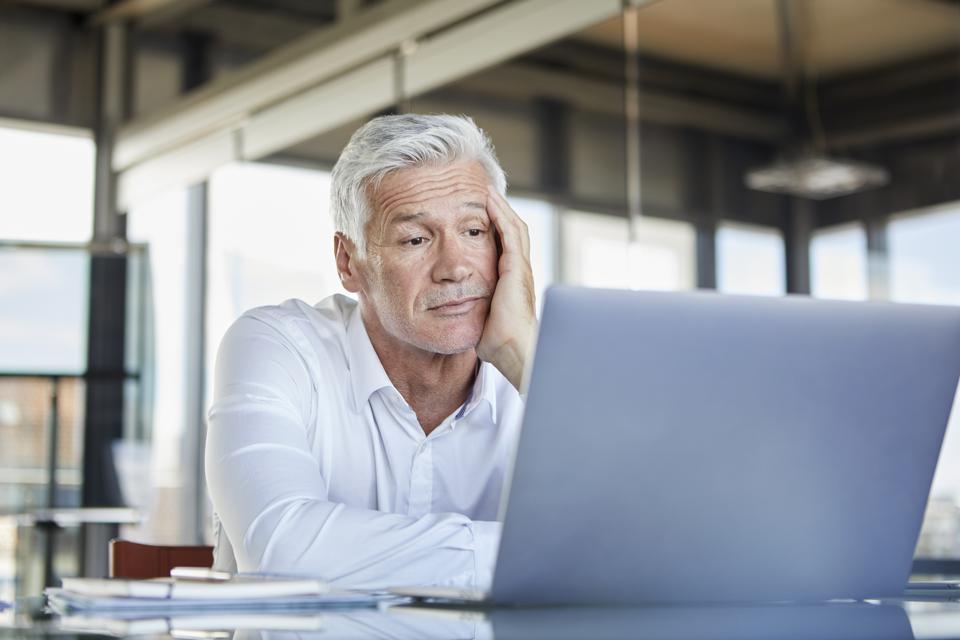 Bored businessman sitting at desk, using laptop